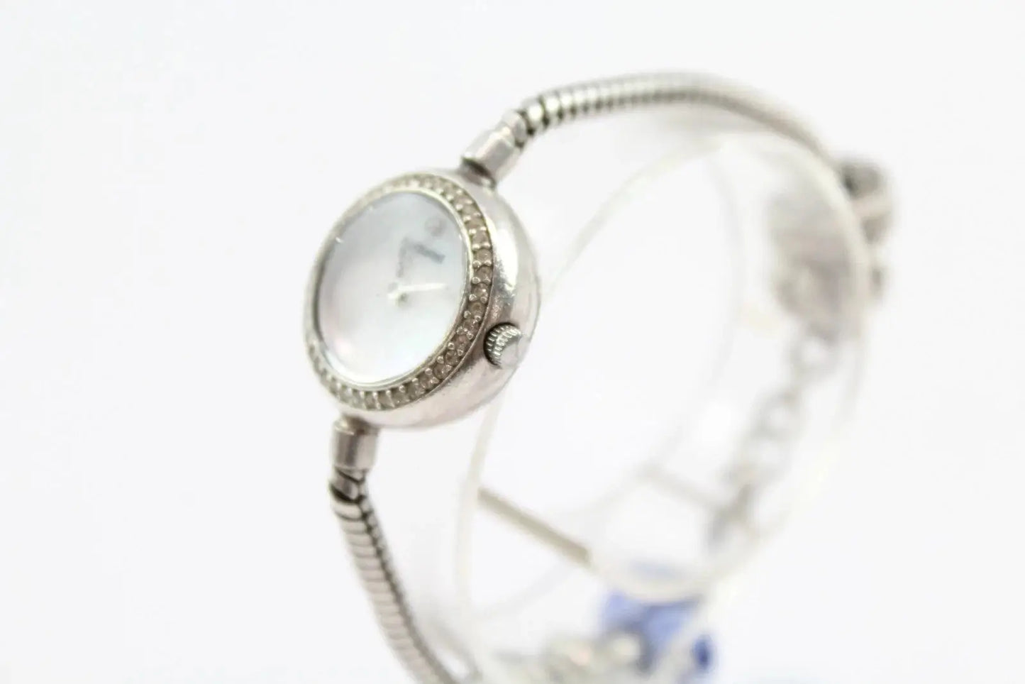A silver-toned watch with a textured bangle strap and a round dial accented with small clear stones, shown on a white background.