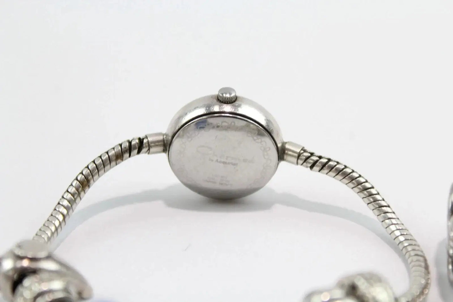 Close-up of the back of a silver-toned watch with a round case and flexible snake-style bracelet on a white background.