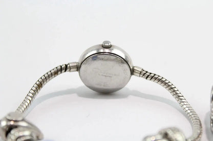 Close-up of the back of a silver-toned watch with a round case and flexible snake-style bracelet on a white background.